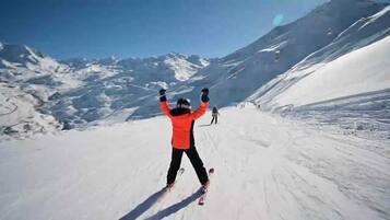Una persona esquiando por una pendiente nevada, con montañas al fondo.