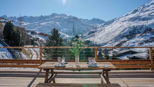 A wooden deck with a table set for two, overlooking a snowy mountain landscape. - Alpeen Hotel (Les Belleville)
