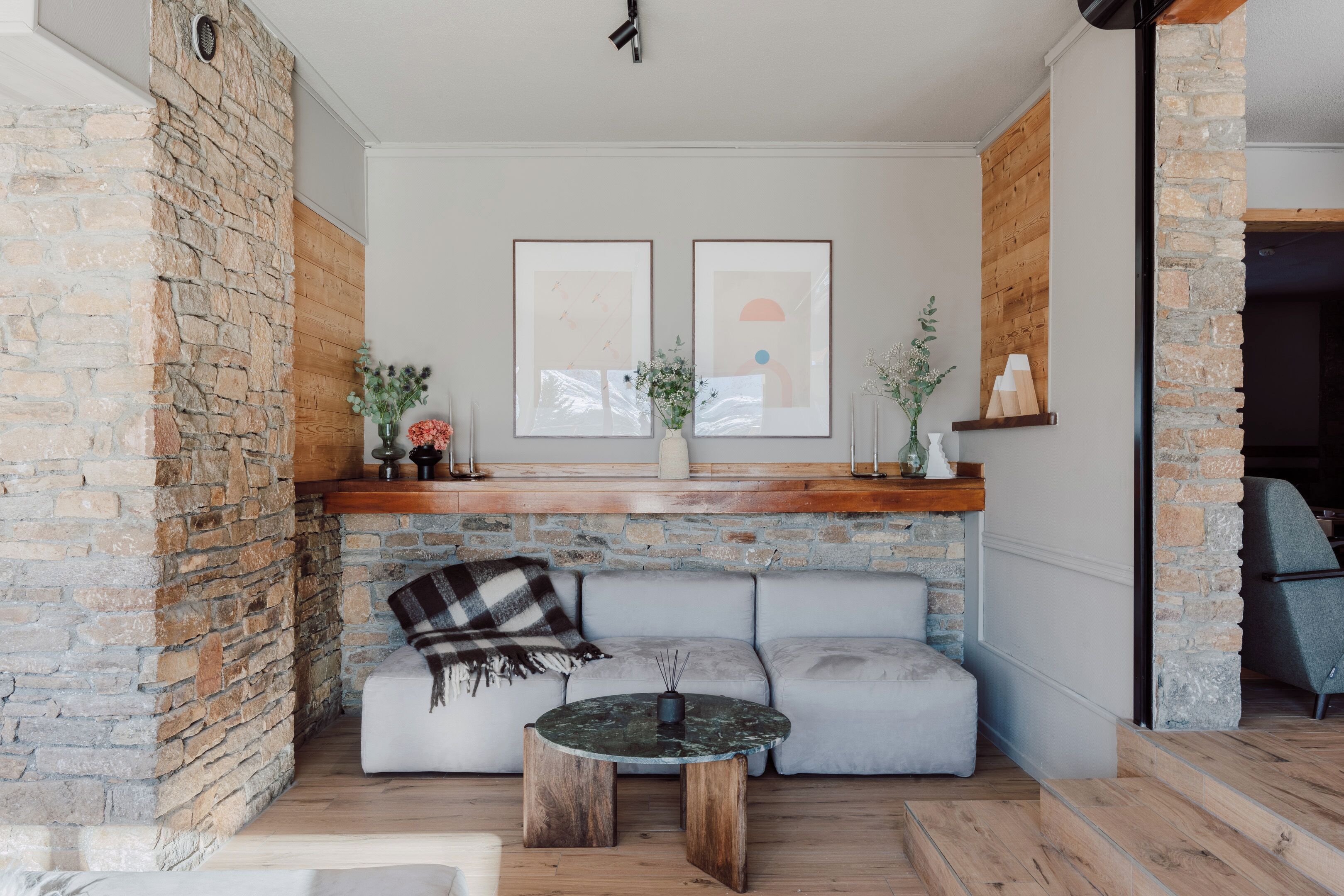 A cozy living area with a stone wall, a gray sofa, a round coffee table, and framed artwork on the wall.