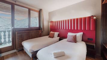 Habitación de hotel con dos camas, cabecero rojo y vistas a las montañas a través de amplios ventanales.