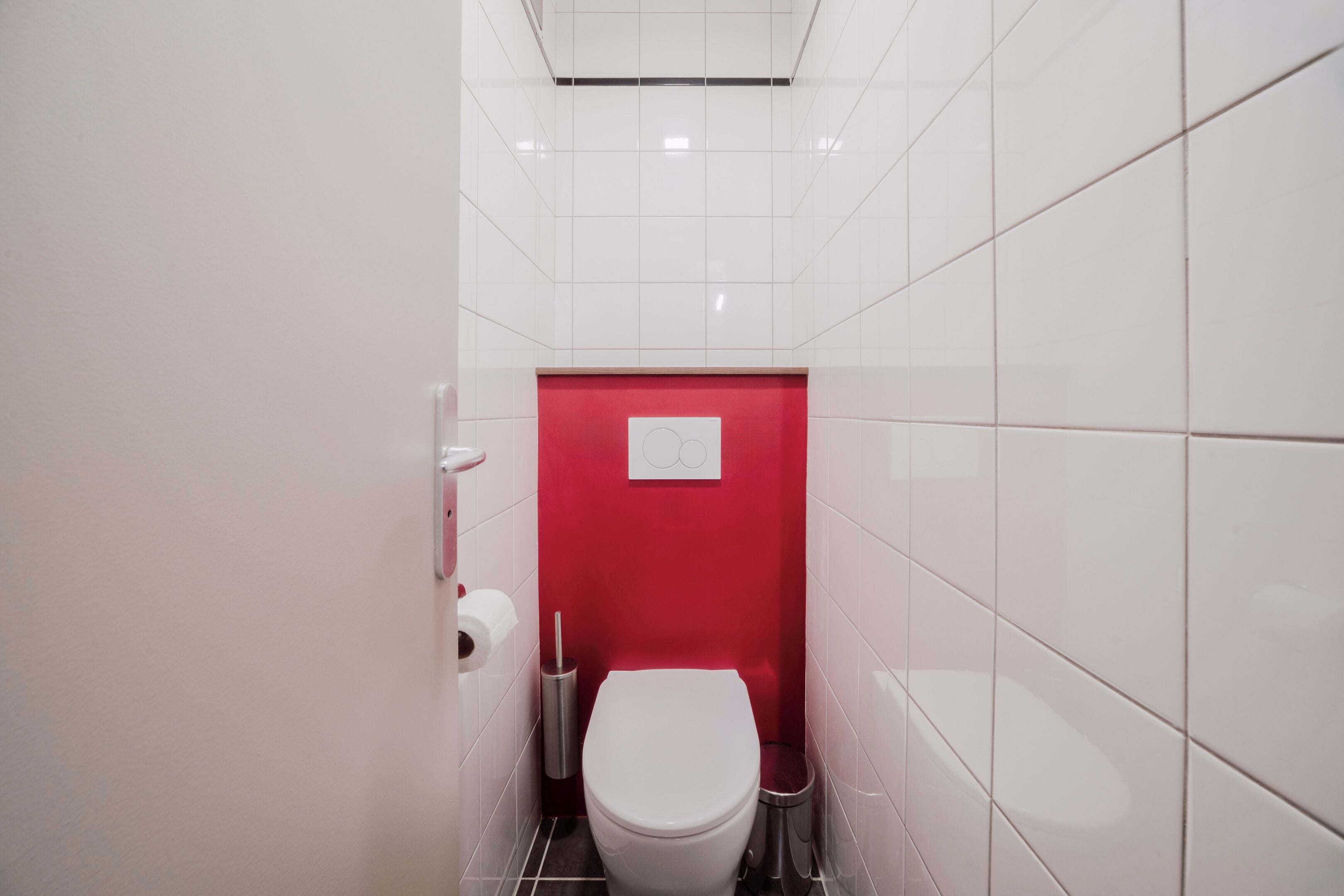 Ein kleines, schmales Badezimmer mit weiß gefliesten Wänden und einer roten Akzentwand.
