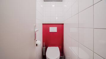 A small, narrow bathroom with white tiled walls and a red accent wall.