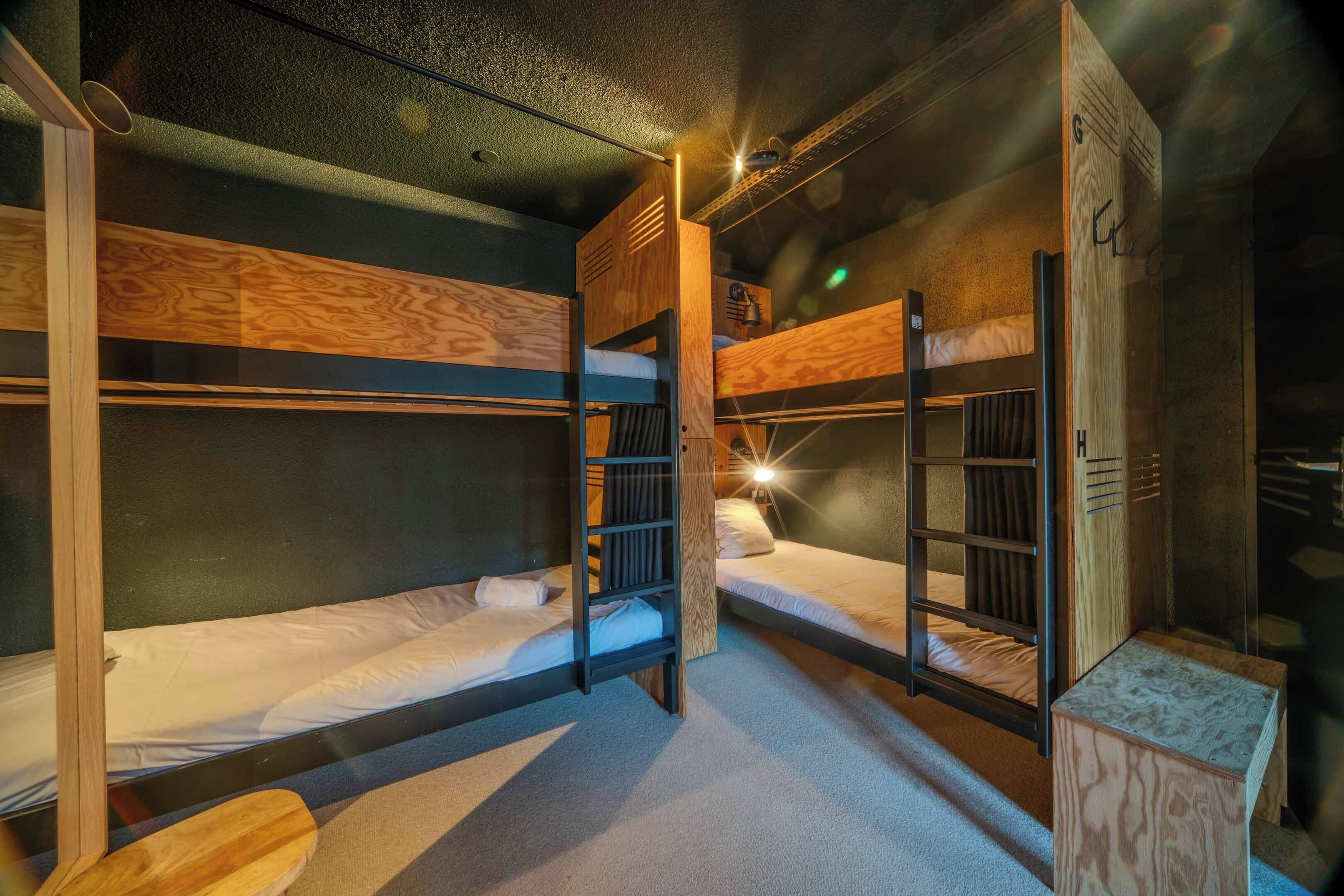 Een kamer met stapelbedden, een ladder en een klein houten tafeltje.