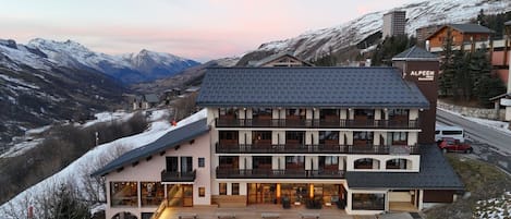 A multi-story hotel with balconies, a wooden deck, and a view of snow-covered mountains.