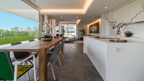 Una cocina moderna con una isla grande, un comedor con mesa y sillas de madera, y vistas a un paisaje verde a través de amplios ventanales.