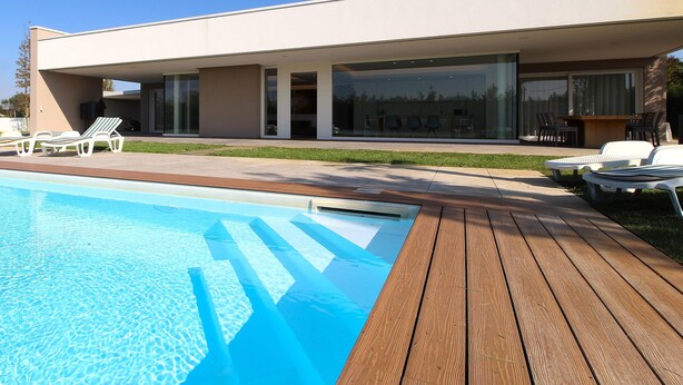 Una casa moderna con piscina, terraza de madera y zona de estar al aire libre.