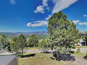 A landscape with a prominent tree in the foreground, a clear blue sky, and distant mountains.