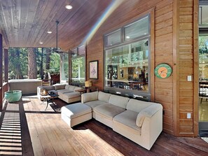 A modern living room with a large sectional sofa, wooden flooring, and large windows offering a view of the outdoors. - Blue Duck Lodge | River View, Pet-Friendly (Ruidoso)