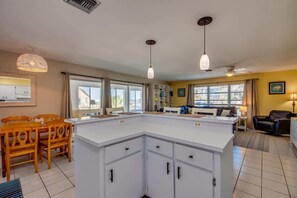 A modern kitchen with white cabinets, a dining area with wooden chairs, and a living room with a sofa and a coffee table.