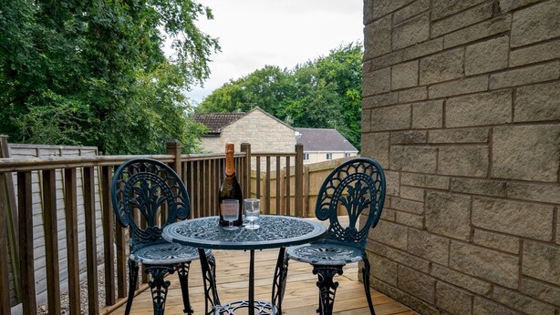 A wooden deck with a round table and four chairs, a bottle of champagne, and a glass on the table. - 3 Bedroom family home | Parking | Garden - Pass the Keys (Stroud)