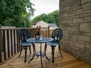 Una terraza de madera con una mesa redonda y cuatro sillas, una botella de champán y una copa sobre la mesa.