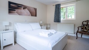 A neatly arranged bedroom with a large bed, bedside tables, a radiator, and a window with curtains. - 3 Bedroom family home | Parking | Garden - Pass the Keys (Stroud)