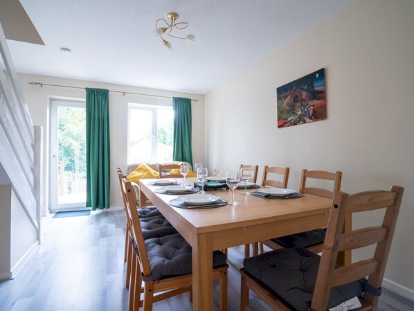 Comedor con mesa de madera dispuesta para cuatro personas, rodeada de sillas con cojines.