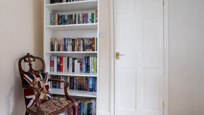 A room with a bookshelf filled with books, a wooden chair with a floral pattern, and a white door. - 3 Bedroom family home | Parking | Garden - Pass the Keys (Stroud)