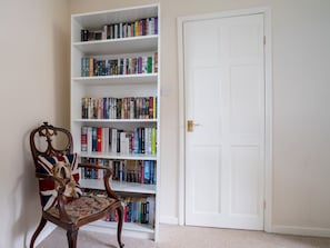 Une pièce avec une bibliothèque remplie de livres, une chaise en bois à motifs floraux et une porte blanche.