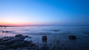 Ein ruhiger See im Abenddämmerung mit Felsen und vereinzelter Vegetation.