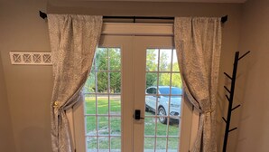 Ein Zimmer mit Doppeltür, Kleiderständer, Teppich und Fenster mit Blick auf ein Auto und Grünfläche.