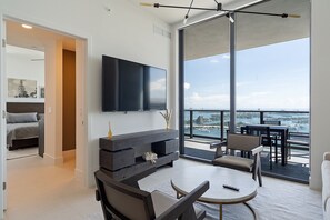 Ein modernes Wohnzimmer mit großem Fernseher, Kamin und Balkon mit Meerblick.