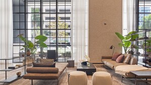 A modern living room with a sofa, ottomans, a coffee table, and large windows with a view of buildings and trees. - Exclusive 3BD Penthouse on 50th Floor,  Direct Water & City Views (Miami)