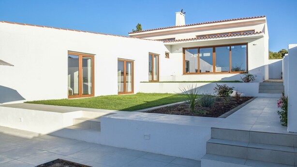Ein modernes, zweistöckiges Haus mit weißer Fassade, großen Fenstern und einem kleinen Garten.