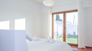 Ein Schlafzimmer mit einem großen Bett, einem Nachttisch und Blick auf einen Garten durch eine Schiebetür.