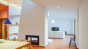 Ein modernes Wohnzimmer mit Kamin, einem Essbereich mit Tisch und Stühlen sowie einem weißen Sofa im Hintergrund.