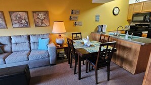 A cozy living room with a sofa, a coffee table, and a dining area with chairs and a table. There is a kitchen area with a microwave and a sink. - Cozy, Clean & Comfortable Condo, less than 2 miles to Silver Dollar City (Reeds Spring)