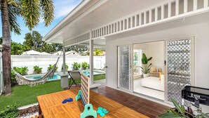 Ein modernes Haus mit einer Holzterrasse, einer Hängematte, einem Pool und einer Glaswand, die zu einem Wohnbereich führt.