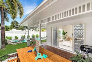 Una casa moderna con una terrazza in legno, un'amaca, una piscina e un'ampia vetrata scorrevole che dà su un soggiorno.