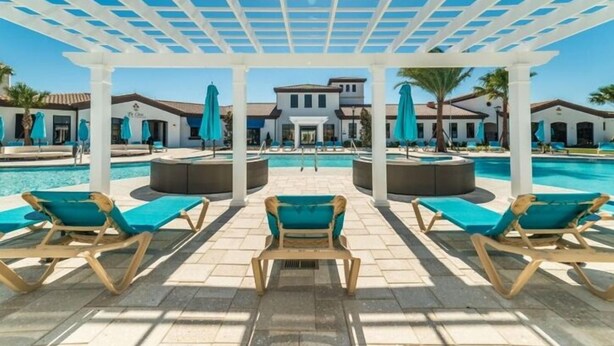 Un área junto a la piscina con sillones de descanso y sombrillas, una pérgola en la parte superior y una piscina al fondo.