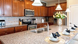 Cocina con armarios de madera, electrodomésticos de acero inoxidable, encimeras de granito y una isla central con pileta y comedor.