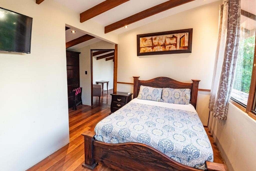 A bedroom with a wooden bed, a TV mounted on the wall, and a painting above the bed.