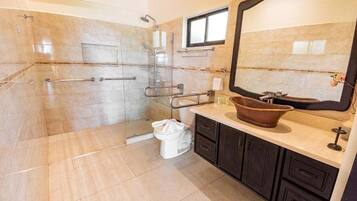 Un baño con cabina de ducha de vidrio, inodoro blanco, lavabo con espejo grande y muebles de color oscuro.