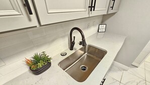 Una cocina con armarios blancos, un lavamanos de acero inoxidable y una pequeña planta en maceta sobre la encimera.
