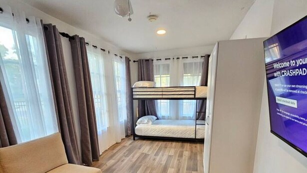 Una habitación de hotel moderna con literas, un televisor de pantalla plana, un ventilador de techo y un sofá.