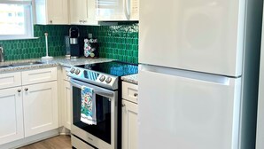 A kitchen with white cabinets, a stainless steel stove, a white refrigerator, and green decorative leaves on the ceiling.