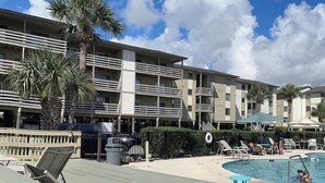A hotel with outdoor pool, lounge chairs, and palm trees.