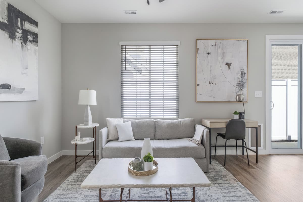 A modern living room with a grey sofa, a white coffee table, and a desk with a chair.