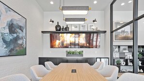 Une salle de conférence moderne avec une longue table en bois, des chaises à revêtement gris, un grand tableau abstrait, une cheminée et un mur de verre offrant une vue dégagée.