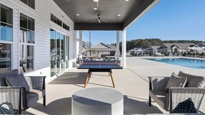 Un espace extérieur abrité comprenant une table de ping-pong, des sièges et une piscine en arrière-plan.