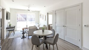 A modern living room with a dining area, a ceiling fan, and a large window. - Landing Apartments Huntsville (Huntsville)