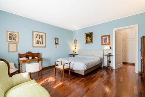 Una camera da letto con un letto, due sedie, una scrivania e quadri appesi al muro.