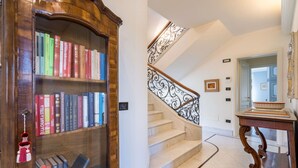 A grand staircase with ornate metal railings, a wooden bookcase filled with books, and a marble floor. - Villa Le Fontanelle In Forte Dei Marmi (Forte dei Marmi)