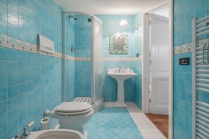 Un bagno con piastrelle blu, un lavandino bianco, un water e una doccia.