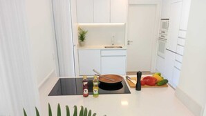 A modern kitchen with white cabinets, a black stove, and a countertop with a frying pan, bottles, and fresh vegetables.
