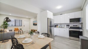 Une cuisine moderne avec des meubles blancs, des appareils en acier inoxydable et un coin repas comprenant une table et des chaises en bois.