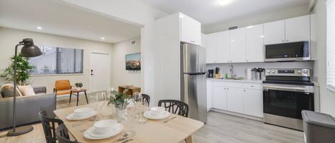 A modern kitchen with white cabinets, stainless steel appliances, and a dining area with a wooden table and chairs.