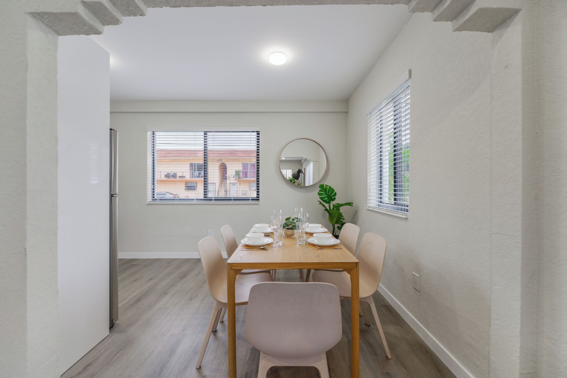Un comedor con una mesa dispuesta para cuatro personas, un espejo redondo y una planta en maceta.