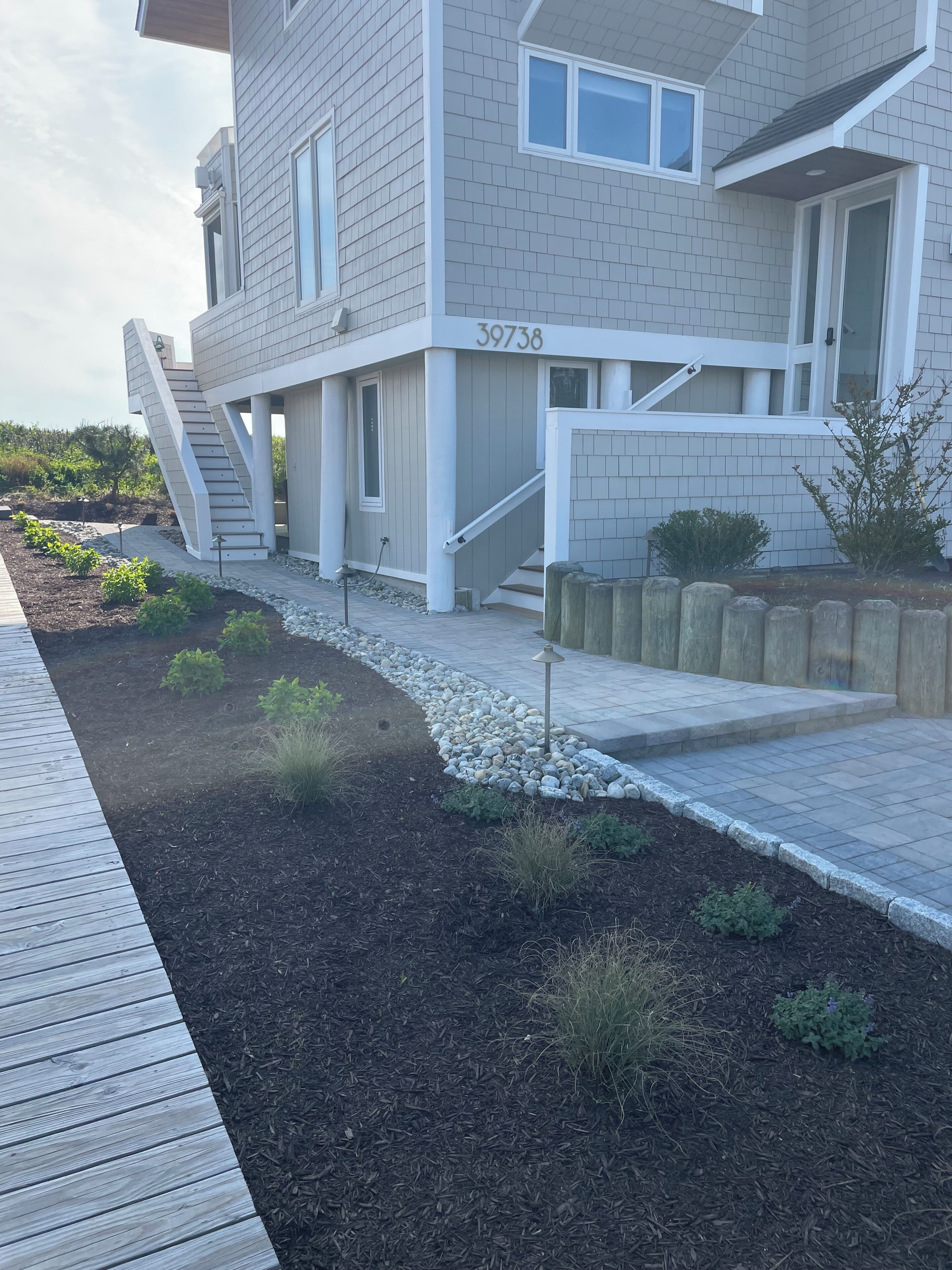 Ein modernes Haus mit einem einzigartigen Treibwerdesign, Nummer 39738, und einem gepflegten Garten mit Mulch und kleinen Pflanzen.