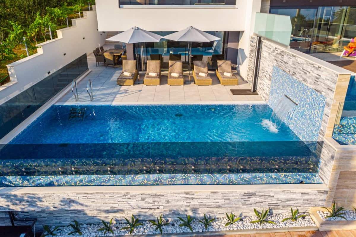A modern pool area with a clear blue pool, lounge chairs, and umbrellas.